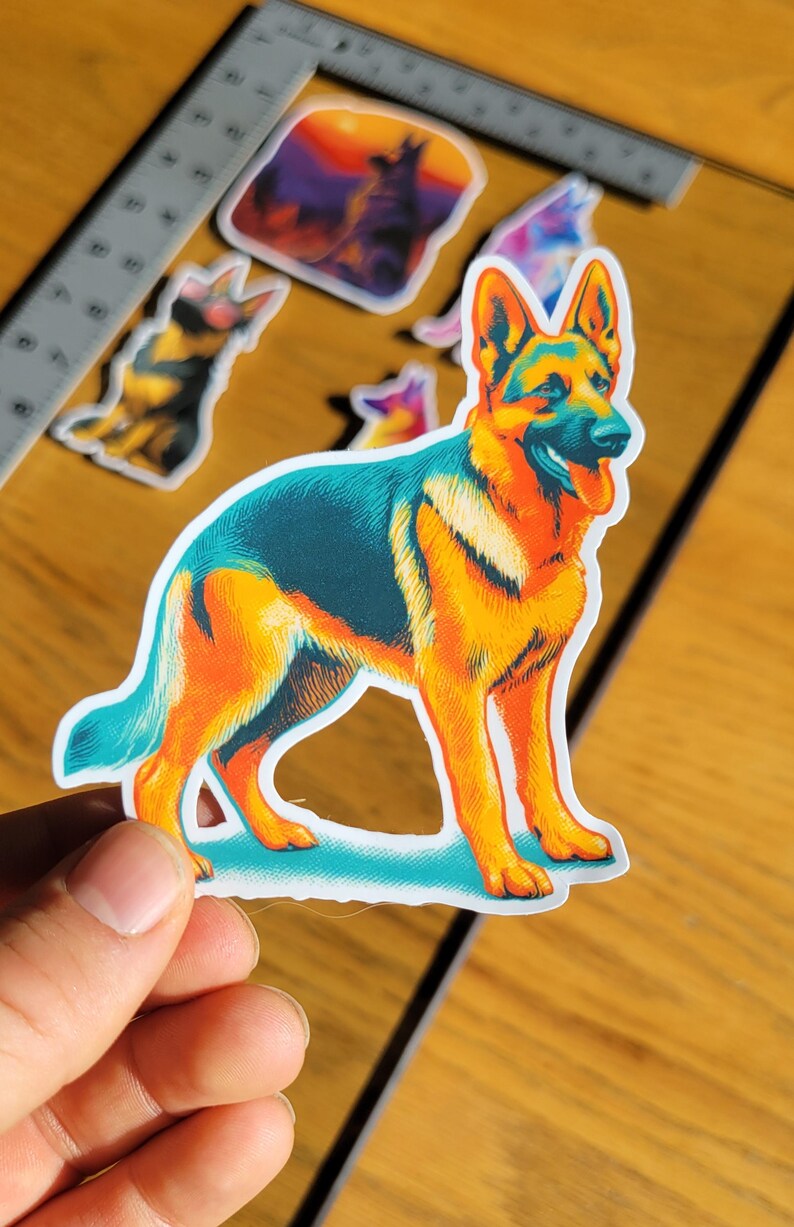 May include: A colorful sticker featuring a stylized German Shepherd dog in a standing pose. The sticker has a vibrant color palette of orange, blue, and yellow. Additional dog-themed stickers are visible in the background.