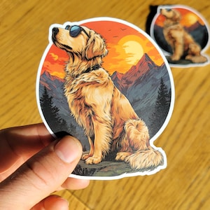 May include: A sticker featuring a golden retriever wearing sunglasses, set against a sunset backdrop with mountains and trees. The dog is the primary focus, with a smaller sticker of the same design visible in the background.