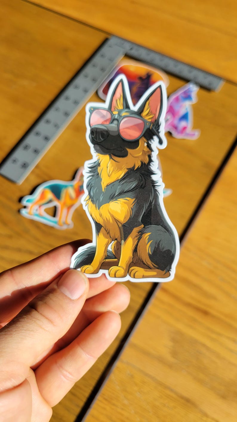 May include: A sticker featuring a cartoon German Shepherd wearing sunglasses with pink lenses. The dog is depicted in black and yellow, sitting upright. Other stickers are visible in the background.