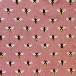 May include: A repeating pattern of yellow and black bees with white wings on a pink background. The bees are evenly spaced across the fabric, creating a visually appealing design. The fabric has a textured appearance.