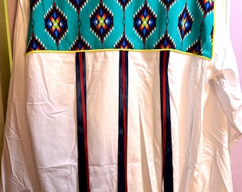 May include: White button-down shirt with a turquoise patterned yoke and vertical ribbons. The yoke features a geometric design in shades of blue, yellow, red, and white, outlined with yellow trim. Ribbons in red and navy blue are attached to the back.