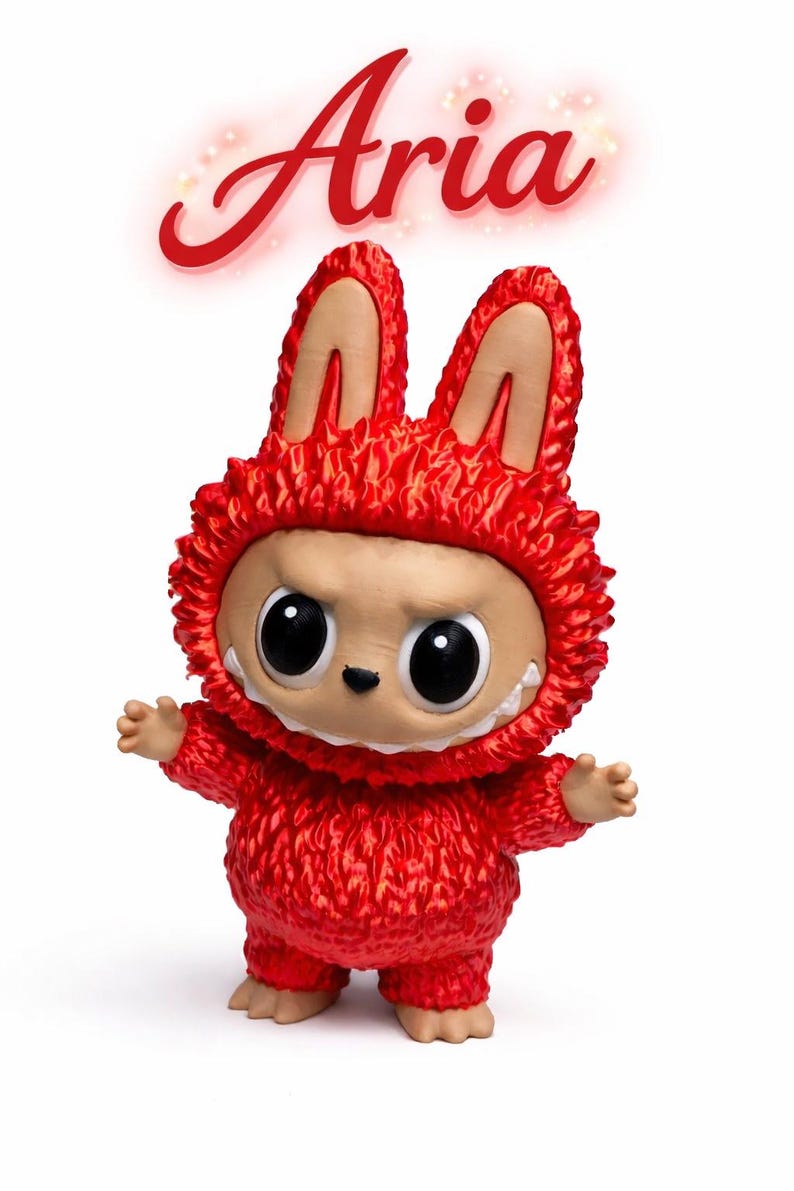 May include: A red figurine of a creature with large eyes, a toothy grin, and a furry red costume with bunny ears. The name "Aria" is written in red script above the figure.