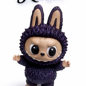 May include: A figurine of a creature with a purple furry suit and large, expressive eyes. The figure has large ears and a toothy grin. The word "Raven" is written above the figure in a stylized font.