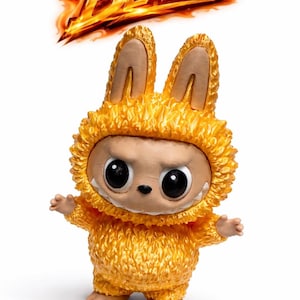 May include: A figurine of a creature in a yellow, furry bunny suit with large, black eyes and a neutral expression. The word "BLAZE" is above the figure in fiery orange text.