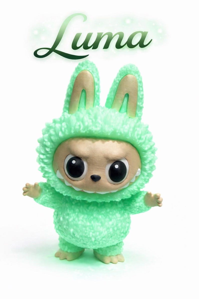 May include: A green plush figure in a bunny costume with the name "Luma" in green script above. The figure has large black eyes, a small nose, and a slightly menacing expression. The costume has a fluffy texture.