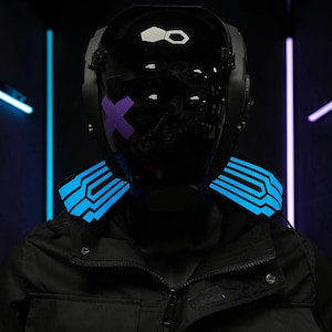 Puede incluir: Un casco futurista negro con un diseño 'X' morado y detalles azules iluminados. El casco tiene un acabado brillante y se lleva sobre una chaqueta negra. El fondo presenta luces de neón azules y moradas.