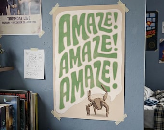 Op de afbeelding: Een rechthoekige muurposter met het woord AMAZE! drie keer herhaald in grote, golvende, groene letters tegen een crèmekleurige achtergrond. Onder de tekst staat een klein, beige wezen met meerdere poten op de poster.