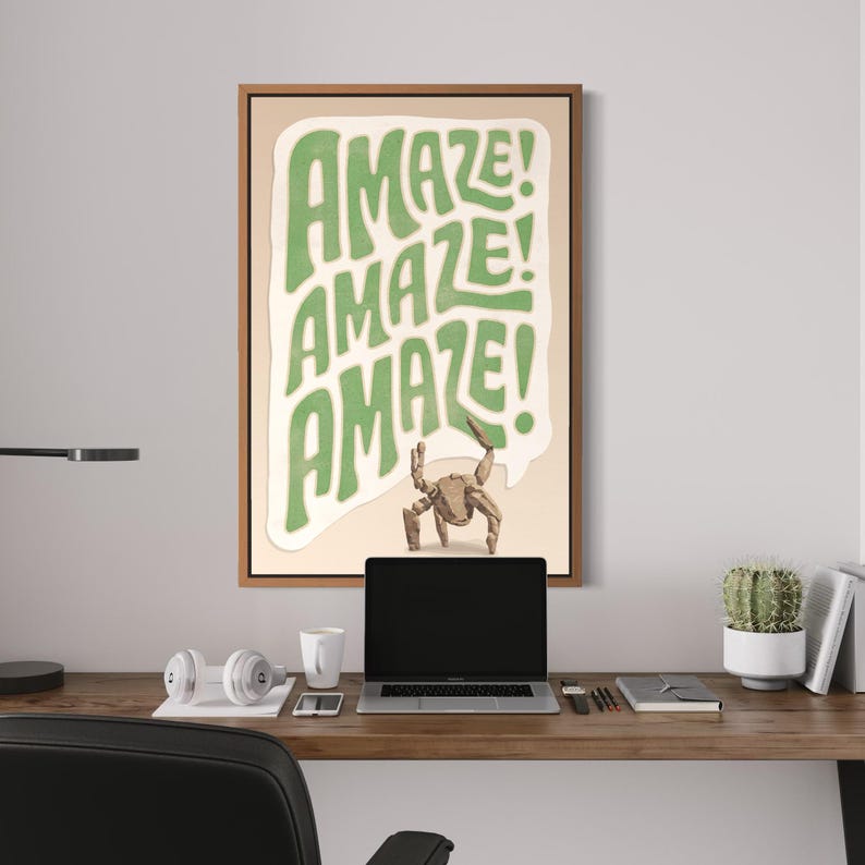 Puede incluir: Una l&aacute;mina de arte mural enmarcada que presenta un bocadillo de di&aacute;logo de color verde claro con la palabra AMAZE! repetida tres veces en una fuente estilizada. Debajo del texto, una peque&ntilde;a ilustraci&oacute;n de un cangrejo marr&oacute;n sobre fondo beige.