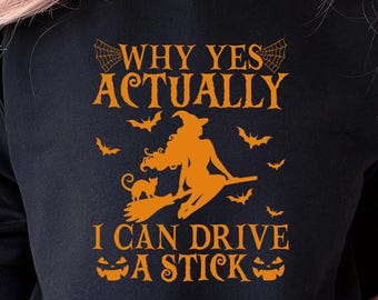 May include: Black sweatshirt with orange text and graphics. The text reads "WHY YES ACTUALLY I CAN DRIVE A STICK" with a witch on a broom, bats, and jack-o'-lanterns. A Halloween-themed design.