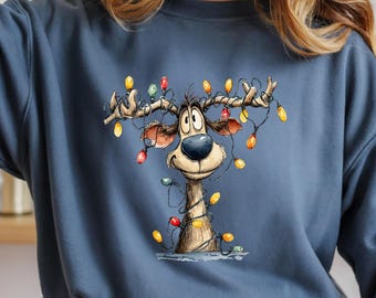May include: Indigo blue sweatshirt featuring a cartoon reindeer decorated with colorful Christmas lights. The reindeer has large eyes and is wrapped in a string of lights. The sweatshirt has a crew neck and long sleeves.