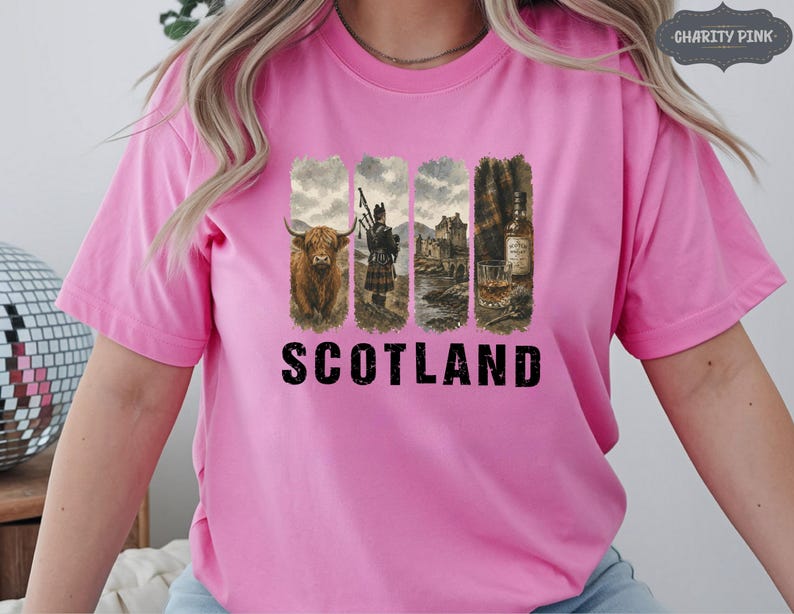 May include: Pink t-shirt featuring a graphic design with four vertical panels. The panels depict a Highland cow, a bagpiper, a castle, and a whiskey bottle and glass. The word "SCOTLAND" is printed in bold black letters.