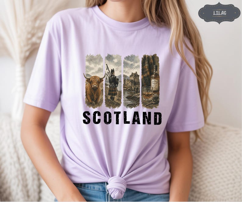 May include: Lilac t-shirt with a graphic featuring Scottish imagery. The design includes a Highland cow, a bagpiper, a castle, and a whiskey bottle with a glass. The word "SCOTLAND" is printed in bold, black letters below the images.