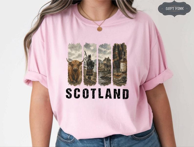 May include: A light pink t-shirt featuring a graphic of Scotland. The graphic includes a Highland cow, a bagpiper, a castle, and a bottle of whiskey. The word "SCOTLAND" is printed in bold black letters below the graphic.