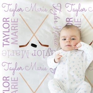 A baby lying on a blanket with the names "Taylor" written on it in purple text.