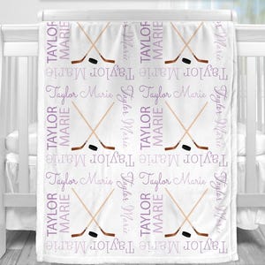 a white crib with a blanket on it, which has a repeating pattern of hockey sticks crossed over each other in purple and white colors.