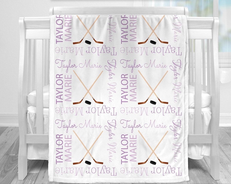 a white crib with a blanket on it, which has a repeating pattern of hockey sticks crossed over each other in purple and white colors.
