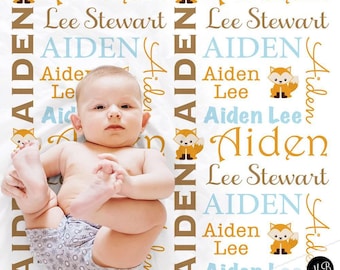 May include: A baby blanket with the name "Aiden" in a repeating pattern with fox illustrations. The blanket also includes the name "Lee Stewart" and the word "AIDEN" in various colors. The baby is wearing a diaper.