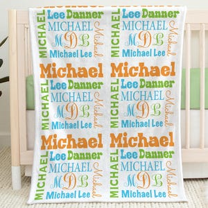 May include: White baby blanket with a repeating pattern of the name "Michael" in orange, blue, and green. The blanket also features the name "Lee Danner" and the initials "MDL".