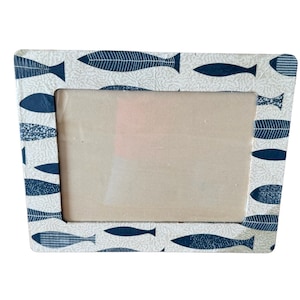 Puede incluir: Marco de fotos rectangular con un patrón repetitivo de peces azules sobre fondo blanco. El marco tiene una abertura rectangular para una foto. El diseño sugiere un tema náutico o costero, adecuado para mostrar una imagen.