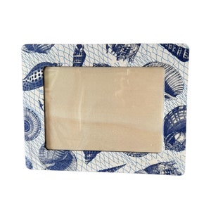 May include: A white picture frame with a blue seashell pattern. The frame has a white background with a blue net pattern and blue seashells.