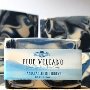 May include: A bar of "Blue Volcano" artisan soap with blue, white, and black swirls, labeled "Handcrafted in Tennessee." The soap is on a natural sponge. The label reads "Sugar Maple South" and "Net Wt. 4-4.5 oz."