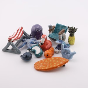 Puede incluir: Una colección de figuras de cerámica coloridas, que incluyen un flamenco, un pulpo, una tabla de surf y una piña. Las figuras están pintadas a mano con colores brillantes y varias formas, perfectas para la decoración del hogar.