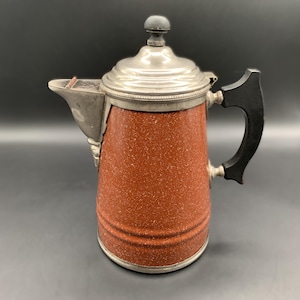 May include: A vintage coffee pot with a speckled reddish-brown exterior and a silver-colored lid and spout. The handle is black, and the pot has a classic design. The pot is likely made of metal and is suitable for brewing coffee.