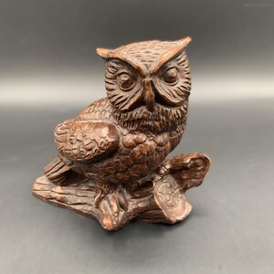 May include: A detailed wooden owl figurine, perched on a carved branch. The owl has intricate feather detailing and a focused gaze. The sculpture is a warm brown color, suggesting a natural wood finish.