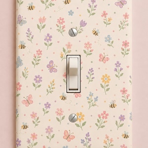May include: A rectangular light switch cover plate featuring a cream background with a repeating pattern of small colourful flowers, butterflies, and bees. The plate has a central toggle switch and two silver screws. The text Honey Meadow is visible.