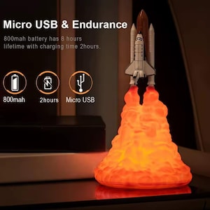 Peut inclure: Lampe décorative en forme de navette spatiale en train de décoller. La lampe présente une navette blanche et marron sur une base orange flamboyante. Le texte "Micro USB & Endurance" est visible, ainsi que des informations sur la batterie.