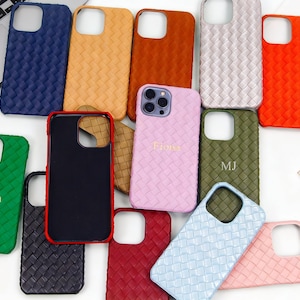 Puede incluir: Una colección de fundas para teléfonos con textura tejida en varios colores, incluyendo azul, naranja, verde y rosa. Algunas fundas tienen texto personalizado. También se ven un portátil, relojes y espigas de trigo decorativas.