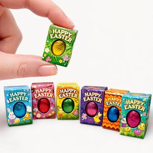 May include: A hand holding a small green box with the words "Happy Easter" and a gold foil-wrapped egg. Several other colorful boxes with foil-wrapped eggs and "Happy Easter" text are arranged below.