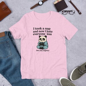 May include: A light pink t-shirt with the text "I took a nap and now I hate everyone less (but only slightly)". The shirt features a cartoon panda wearing a blue and white polka dot outfit.
