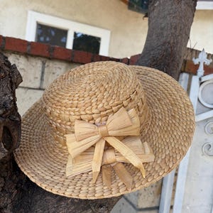 May include: A woven straw sun hat with a wide brim and a decorative bow. The hat is a natural beige color and appears to be made of tightly woven straw. The bow is made of the same material.