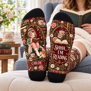 May include: A pair of crew socks with a dark red background featuring floral patterns, stacks of books, and teacups. One sock shows a person reading in a chair with a cat, labelled Chloe. The other sock features the text SHHH... I'M READING.