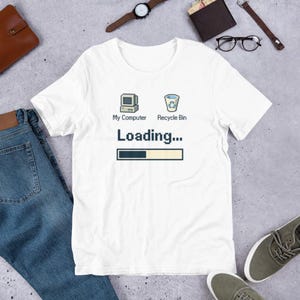 Könnte beinhalten: Weißes T-Shirt mit einem Retro-Computer- und Papierkorb-Grafik. Der Text lautet "My Computer" und "Recycle Bin" über "Loading..." mit einem Fortschrittsbalken. Das Shirt besteht aus einem weichen Material und ist für den Freizeitgebrauch geeignet.