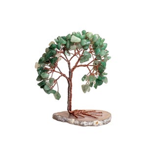 Op de afbeelding: Een decoratieve boomsculptuur met een koperdraadstam en takken, versierd met groene edelsteenbladeren. De boom staat op een natuurlijke, lichtgekleurde stenen basis. Het ontwerp is een unieke mix van natuurlijke elementen en vakmanschap.