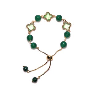 May include: Adjustable gold-tone bracelet featuring green round beads and clover-shaped accents. The bracelet has a sliding clasp for a custom fit and two dangling green beads at the end. The clover accents are a lighter shade of green.