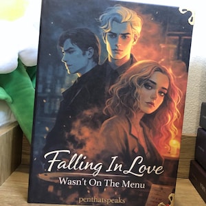 May include: A hardcover book titled "Falling In Love Wasn't On The Menu" with a cover illustration of three people. The cover art features a woman with curly hair and two men against a fiery background. The author's name, penthatspeaks, is also visible.