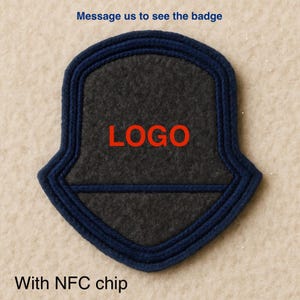 Puede incluir: Una insignia en forma de escudo con un centro gris oscuro y un borde azul marino. La palabra "LOGO" está impresa en rojo en el centro. También se ve el texto "Message us to see the badge" y "With NFC chip".