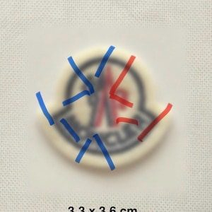 May include: A circular patch with a blurred logo design, featuring blue and red lines drawn across it. The patch measures 3.3 x 3.6 cm.