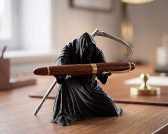 May include: A black figurine of a hooded grim reaper figure kneeling and holding a brown wooden fountain pen with gold-colored accents. The figure has a silver-colored scythe resting behind its back, extending over the shoulder.