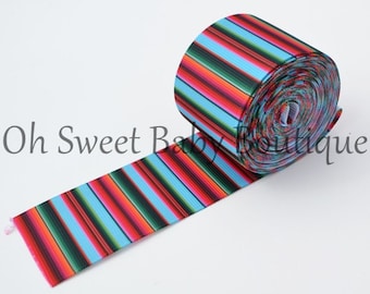 May include: A roll of colorful striped ribbon with red, blue, green, and black stripes. The ribbon is on a white surface.