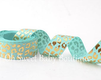 May include: A roll of turquoise blue ribbon with a gold leopard print. The ribbon is 1.5 inches wide.