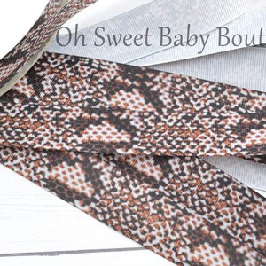 May include: Close-up of several ribbons. One ribbon features a brown, black, and white snakeskin pattern. Other ribbons are white with a subtle ribbed texture. The text "Oh Sweet Baby Boutique" is visible in the background.