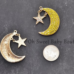 May include: Two gold-tone crescent moon charms with dangling star charms. One moon charm is decorated with yellow rhinestones, the other with a textured surface.