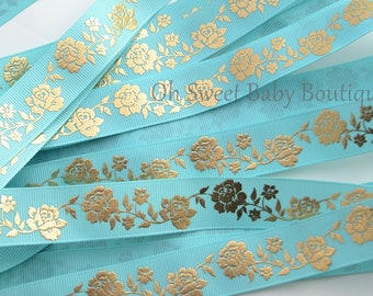May include: Aqua blue ribbon with a gold floral pattern. The ribbon is folded and stacked, showing the pattern repeating.