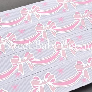 May include: White ribbon with a pink and white bow design. The ribbon has a repeating pattern of bows with streamers.