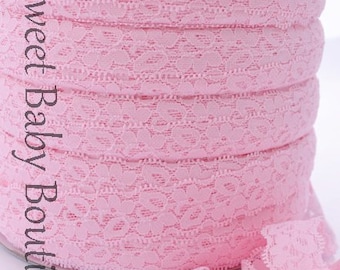 May include: A spool of pink elastic lace trim with a heart pattern. The lace is rolled up on a white cardboard spool.