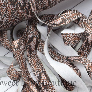 May include: Brown and white patterned elastic with a white backing. The elastic is folded and twisted, showing the pattern on both sides.